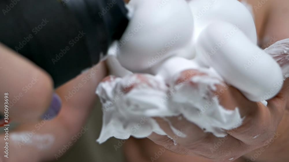 Close-up of a young man's hands squeezing shaving foam from a bottle onto a palm during preparation for shaving. Hair removal in men Close-up of a young man's hands squeezing shaving foam from a bottle onto a palm during preparation for shaving. Hair removal in men