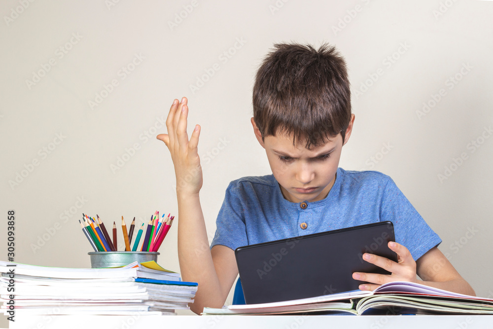 Sad confused child with tablet computer sitting at table with books notebooks Sad confused child with tablet computer sitting at table with books notebooks