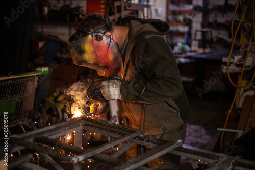 A welder is cooking metal in a protective mask. High temperature of heating.