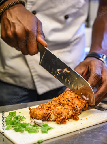 Chef at work cutting breaded chicken with big knife close up.