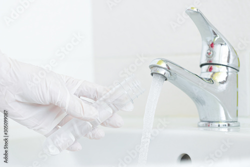 Tap water analysis quality control concept. Hand with a flask and water tap ckose up.