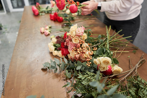 Step by step florist woman creates red beautiful bouquet of mixed flowers. Handsome fresh bunch. Education, master class and floristry courses. Flowers delivery. European floral shop concept.