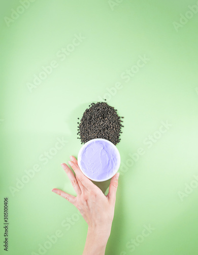 Woman's hand holding purple moisturizing cream with bakuchiol ingredient. Babchi seeds (Psoralea corylifolia). Bakuchiol cosmetics concept. Flat lay, copy space, vertical. photo