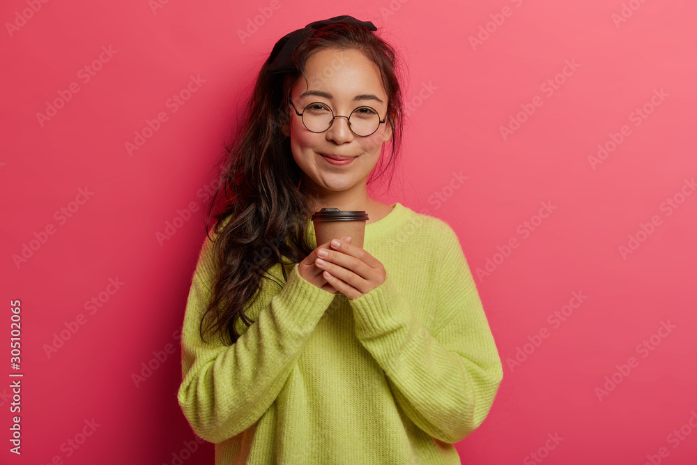 Portrait of attractive korean girl stands with takeaway coffee, enjoys caffeine beverage, looks with tender happy expression, has break, dressed in oversized green jumper drinks hot tea from paper cup Portrait of attractive korean girl stands with takeaway coffee, enjoys caffeine beverage, looks with tender happy expression, has break, dressed in oversized green jumper drinks hot tea from paper cup