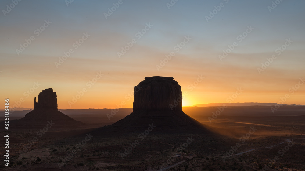 Sun rising behind the Merrik Butte and the Mitten Butte in Monument Valley