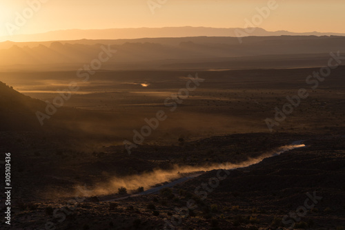 A dusty road thought the desert in Navajo Land. An off-road vehicle crossing through the desert at sunrise