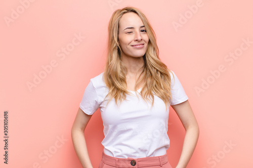 Obraz na plátne young pretty blonde woman looking happy and friendly, smiling and winking an eye