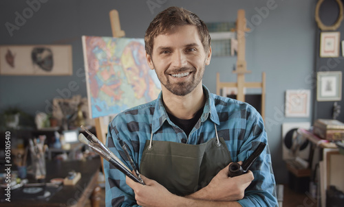 Portrait of young bearded artist in checked shirt with a smoking pipe in a painting atelier