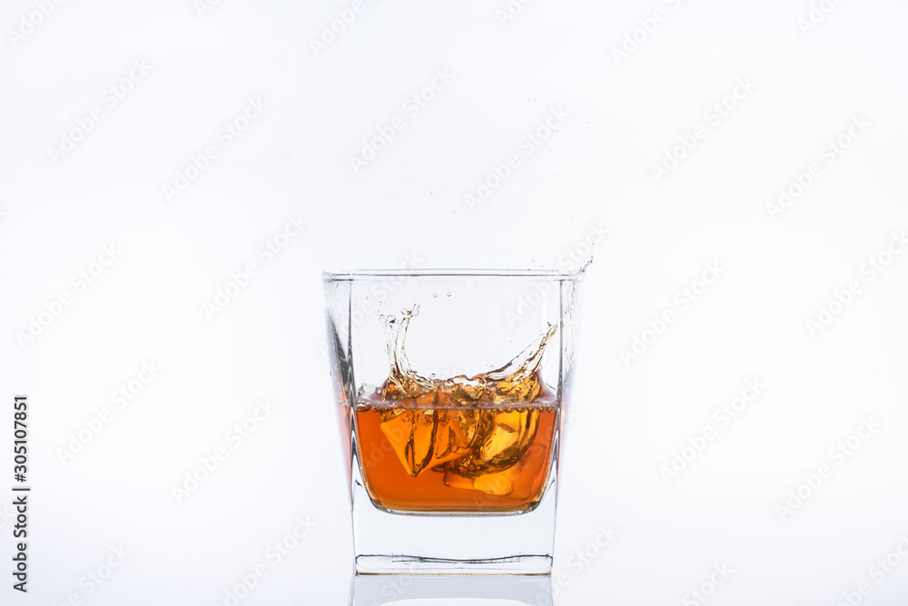 Alcohol in the glass. Whiskey and ice. Rum with ice. Brown brandy with splashes. Ice cube falls into a glass with splashes