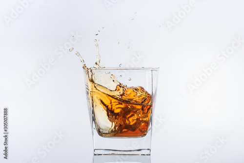 Alcohol in the glass. Whiskey and ice. Rum with ice. Brown brandy with splashes. Ice cube falls into a glass with splashes