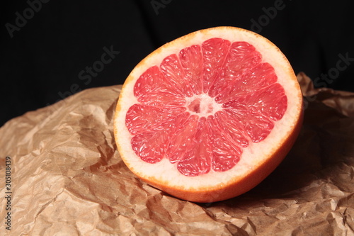 Half of grapefruit on kraft paper and dark background under studio lighting