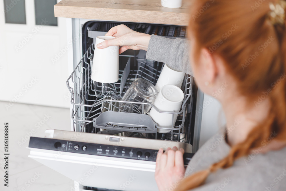 Housework: young woman putting dishes in the dishwasher