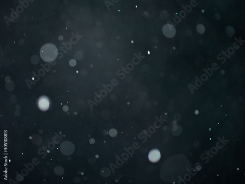 Falling snow or rain bokeh texture on black dark gray background.