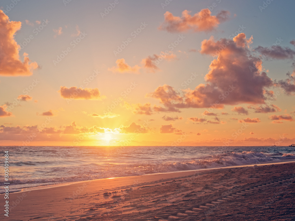 Sunrise over the sea or the ocean. Above the sandy beach is the morning sky with clouds.