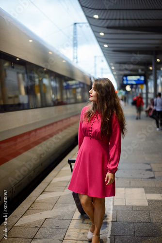 Young girl in red dress goes along the modern train on the railway station, looking for her car