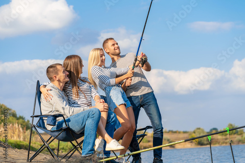 Group of young friends fishing on the pier by lakeside