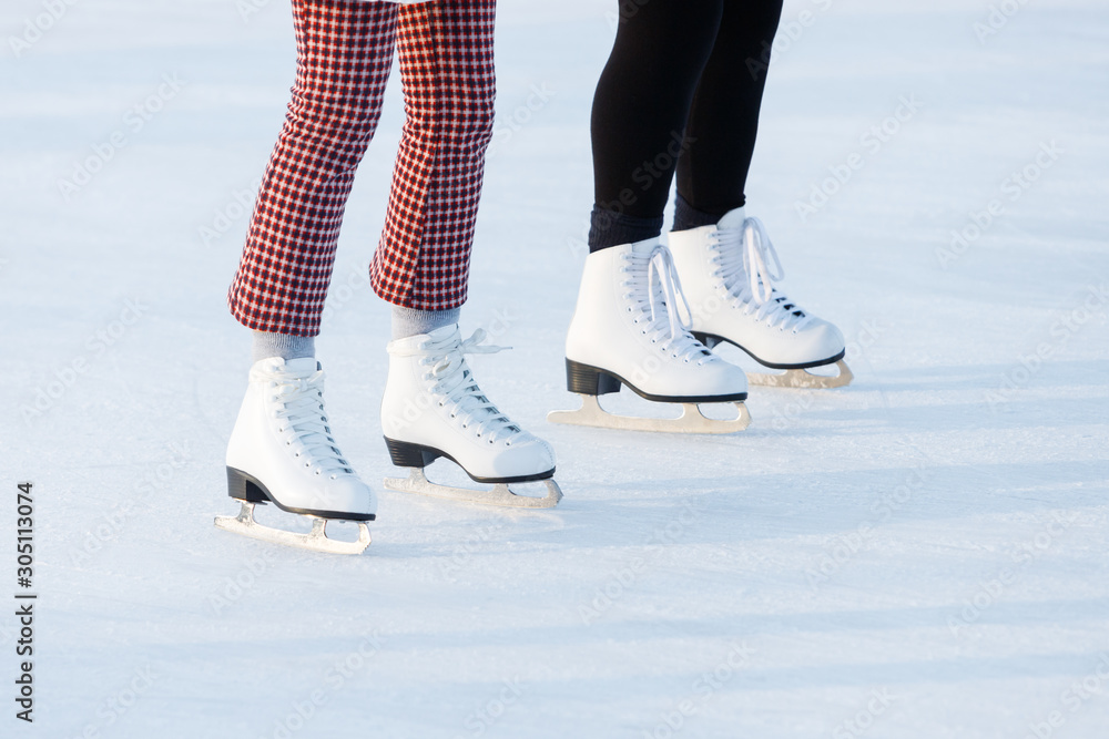 Close up of women's legs on skates in winter on an open skating rink. The ice skates of two friends skating together on a winter afternoon. Winter time, outdoor activities concept Close up of women's legs on skates in winter on an open skating rink. The ice skates of two friends skating together on a winter afternoon. Winter time, outdoor activities concept