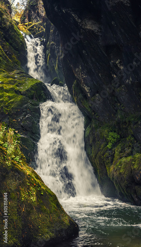 close-up of a mountain waterfall in rocks overgrown with green moss  vertical frame high mountain waterfall