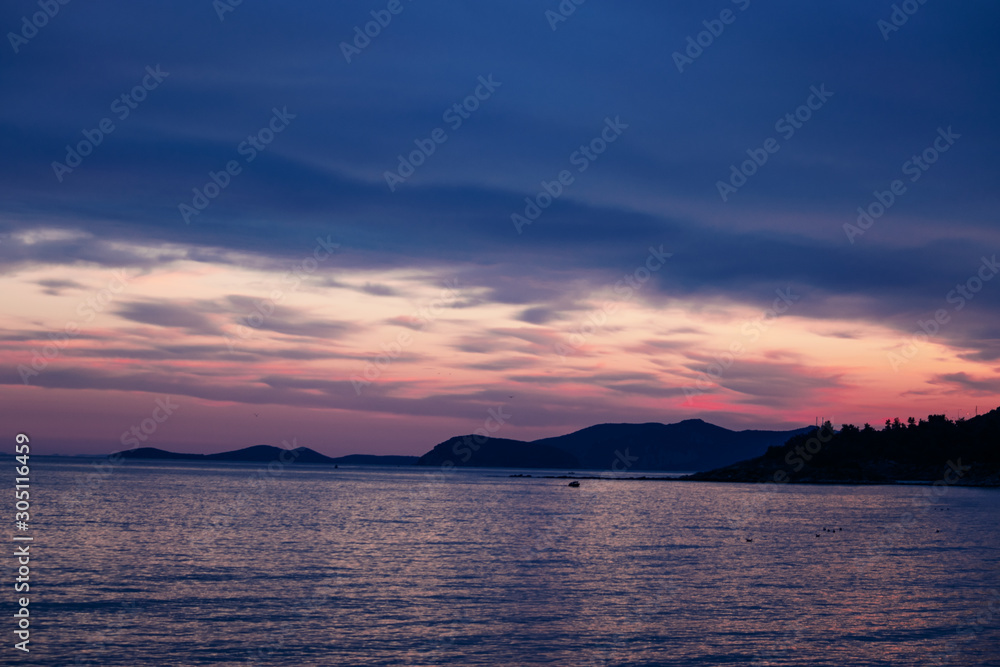 Fototapeta premium Rocky island silhouette in the sea during purple sunset.