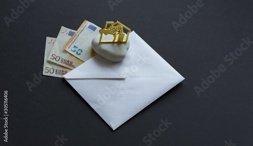 Euro banknotes in white envelope and house figure on black background. Flat lay overhead view. Copy space. Mortgage load concept. photo