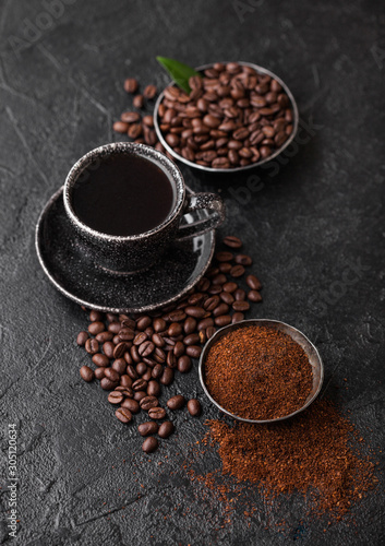 Cup of fresh raw organic coffee with beans and ground powder with cane sugar cubes with coffee tree leaf on black background. Top view