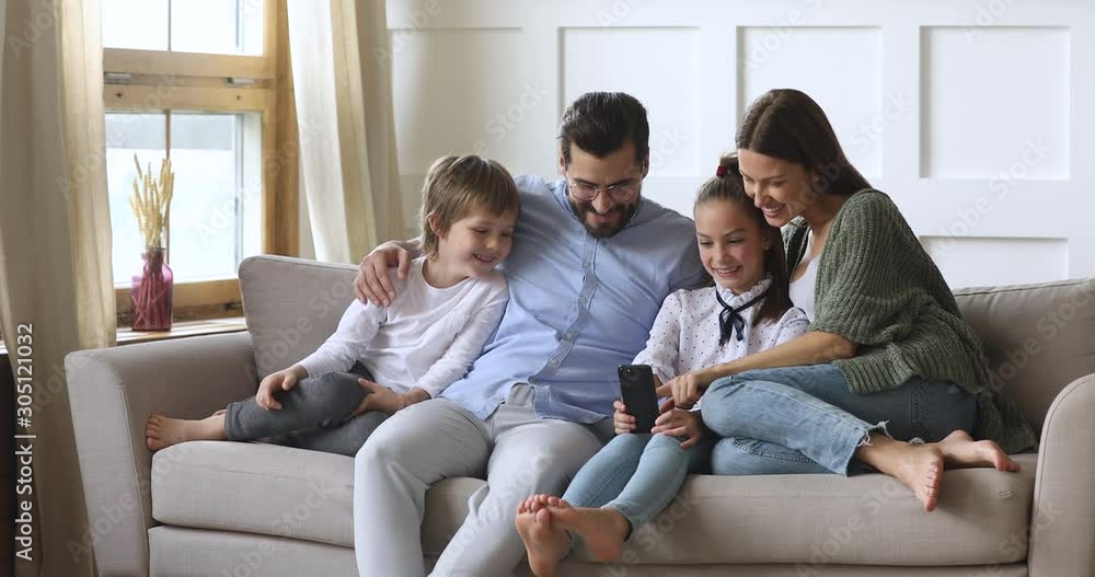 Happy parents with children relax on sofa using smartphone apps Happy parents with children relax on sofa using smartphone apps