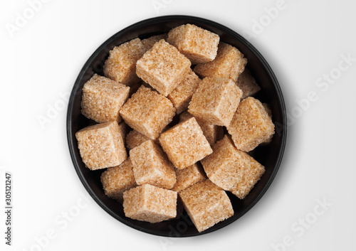 Black bowl plate of natural brown sugar cubes on white background.