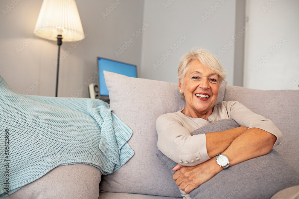 Portrait of beautiful senior woman with white hair. Portrait of senior woman sitting on sofa at home. Smiling middle aged mature grey haired woman looking at camera Portrait of beautiful senior woman with white hair. Portrait of senior woman sitting on sofa at home. Smiling middle aged mature grey haired woman looking at camera