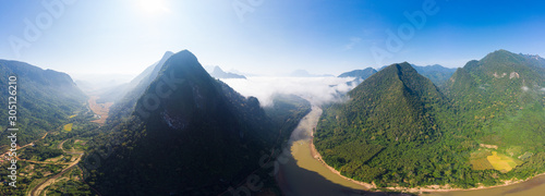 Aerial panoramic Nam Ou River drone flying over morning fog mist and clouds, Nong Khiaw Muang Ngoi Laos, dramatic landscape scenic pinnacle cliff, famous travel destination in South East Asia