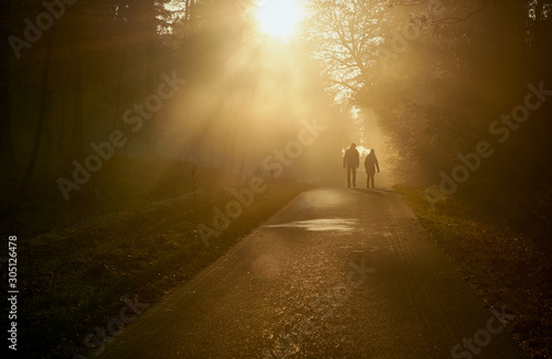 Silhouette of two people walking along a road at sunset.