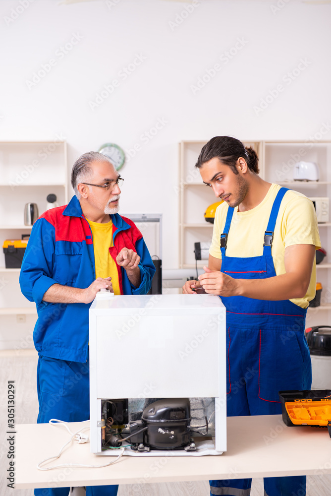 Two contractors repairing fridge at workshop Two contractors repairing fridge at workshop