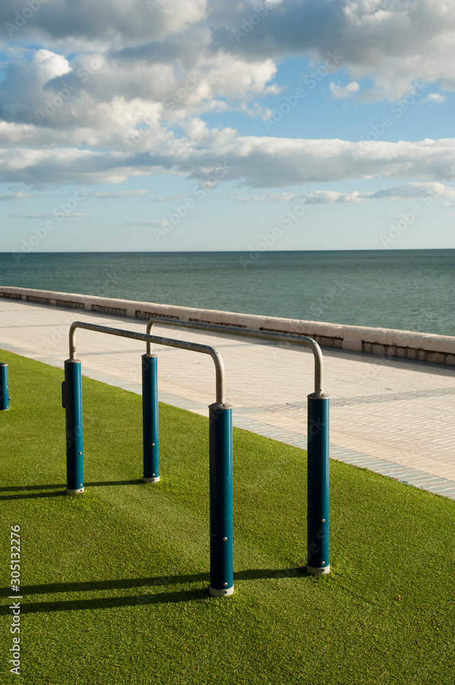 Exercise equipment in a public park on a sunny day with green ground cespe and sea in the background Exercise equipment in a public park on a sunny day with green ground cespe and sea in the background