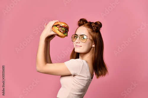 Woman eat burger sandwich with hungry mouth on pink background.