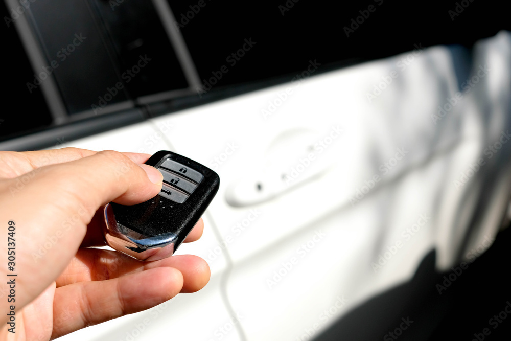 Man hand holding the car remote, he push the remote control to open the car door