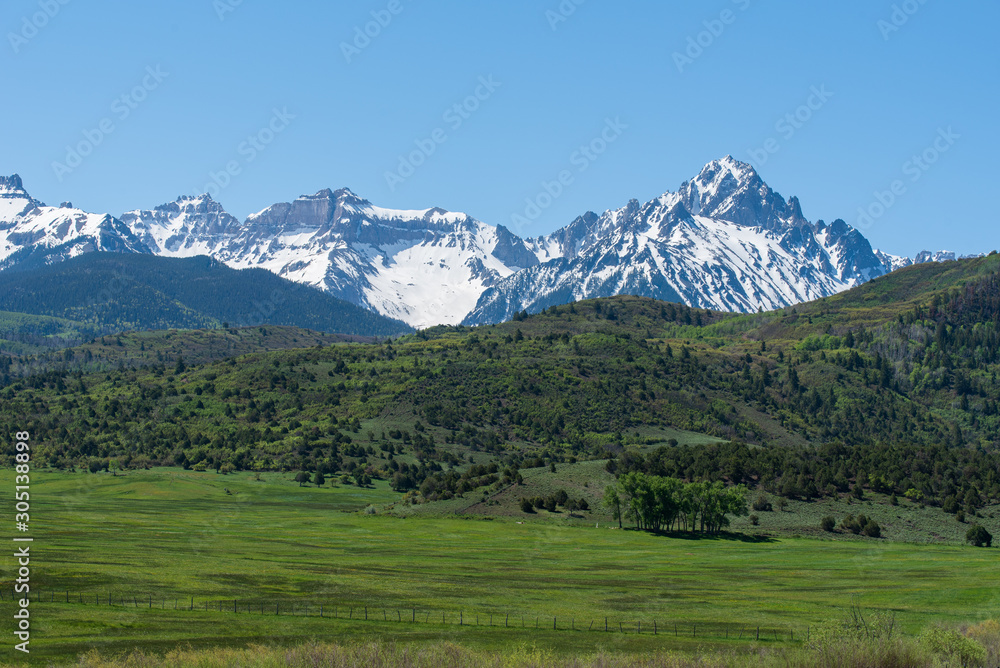 Landscape of meadow, green hillside and snow dappled mountain tops near Ridgway, Colorado