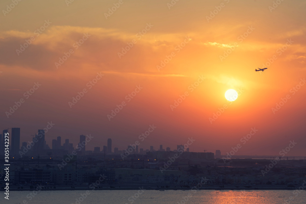 Blurred background image of airplane fly passing colorful sunset over silhouette cityscape view, Bahrain