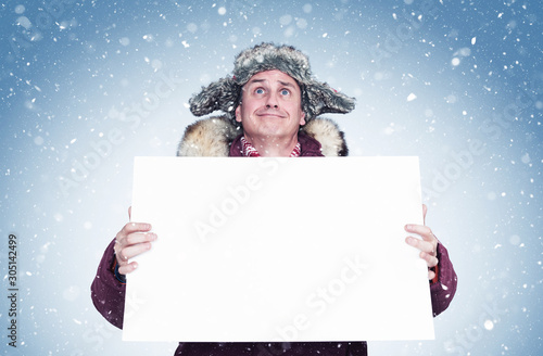 Man in winter clothes looks at the sky and holds a white banner in his hands, snow. 