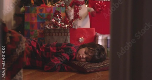 Santa sneaks a present to a sleeping child who stirs by the Christmas tree - slow motion - shot on RED