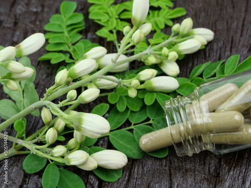 Moringa capsules in glass bottles and leaf flowers on a wooden table.