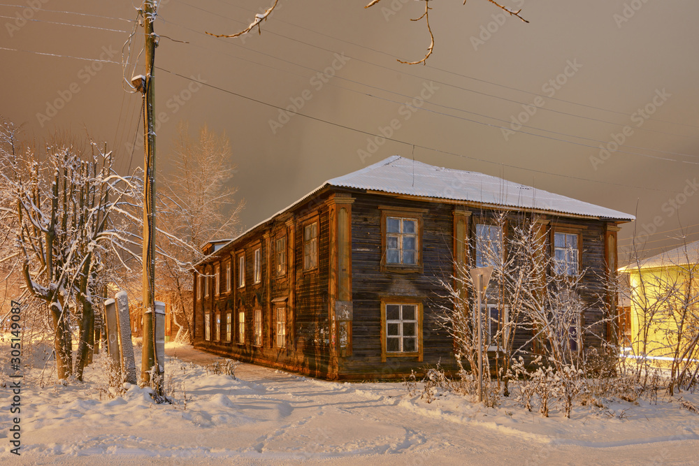 Old wooden house on a snowy frosty street in night illumination