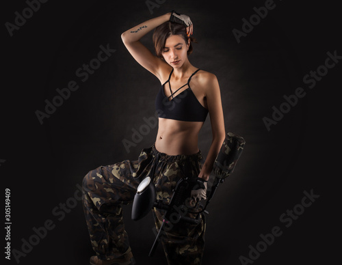 pretty woman in equipment with a paintball gun on a black background. Leisure