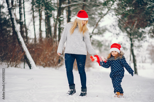 Family have fun in a winter park. Stylish mother in a gray sweater. Little girl in a red hat