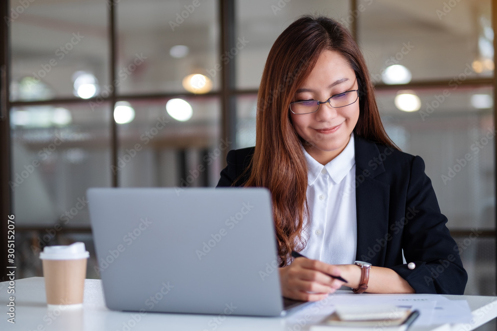 Closeup image of businesswoman writing on notebook and using laptop while working in office Closeup image of businesswoman writing on notebook and using laptop while working in office