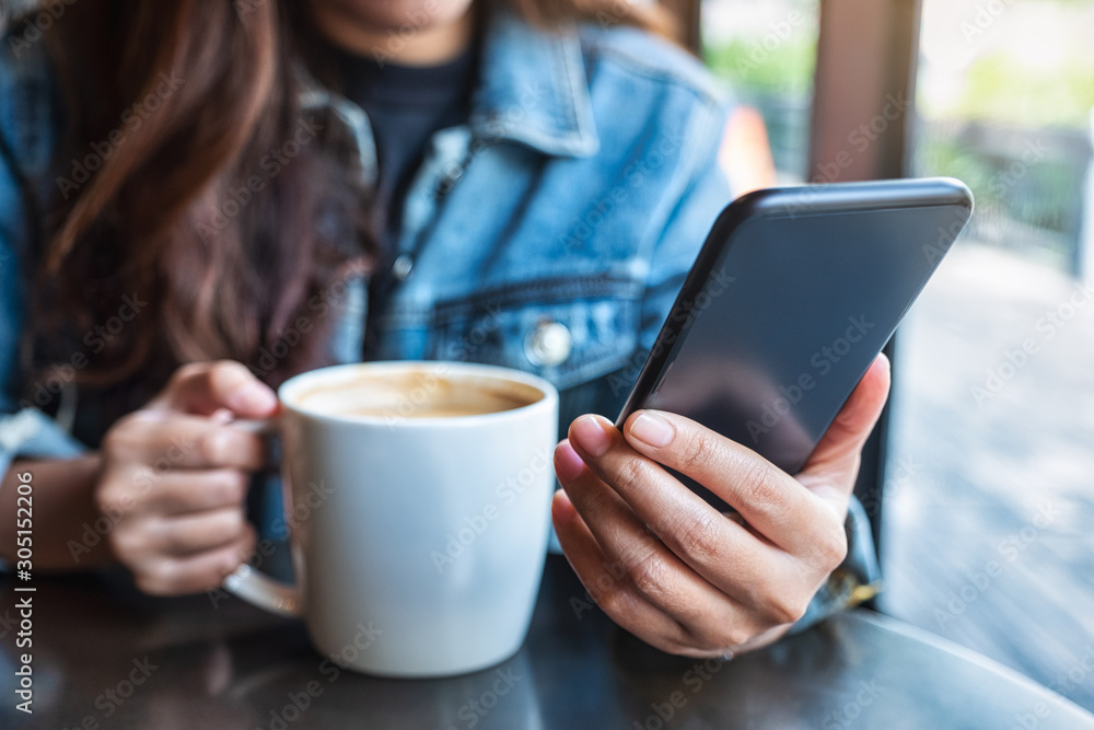 Closeup image of a woman holding and using mobile phone while drinking coffee Closeup image of a woman holding and using mobile phone while drinking coffee