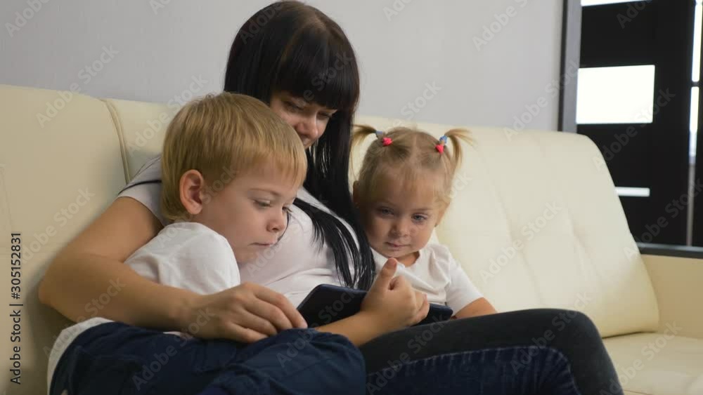 Happy family. Mom with children sits on a sofa with a computer tablet. Family watching a movie. Parenting concept. Teamwork Happy family. Mom with children sits on a sofa with a computer tablet. Family watching a movie. Parenting concept. Teamwork