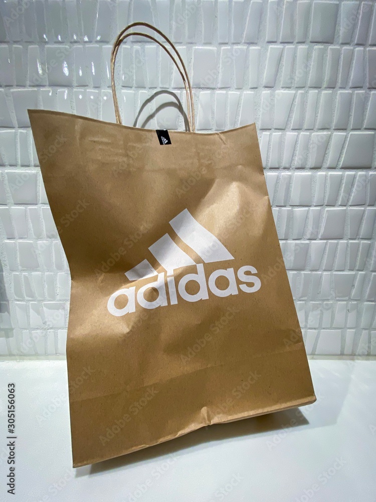 Karuizawa Japan - 23 Nov 2019: Wrinkled paper bag with original Adidas logo  on the tile wall background. Adidas is a large sportswear manufacturer.  foto de Stock | Adobe Stock