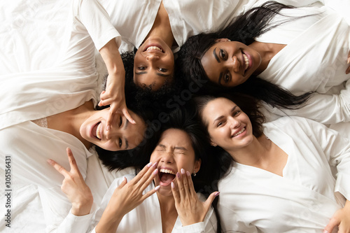 Five happy diverse young girls lying on bed, top view photo