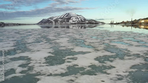 The mountainous sea coast is covered with snow with the sun the closed cloud. Place of shooting northerly coast of the Bering Sea, Chukchi region, Russia.