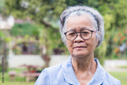 Elderly woman with short white hair standing smiling and looking at the camera in the garden. Senior Asian woman healthy and have positive thoughts on life make her happy every day