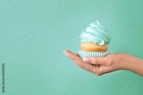 Photography Female hand with tasty cupcake on turquoise background